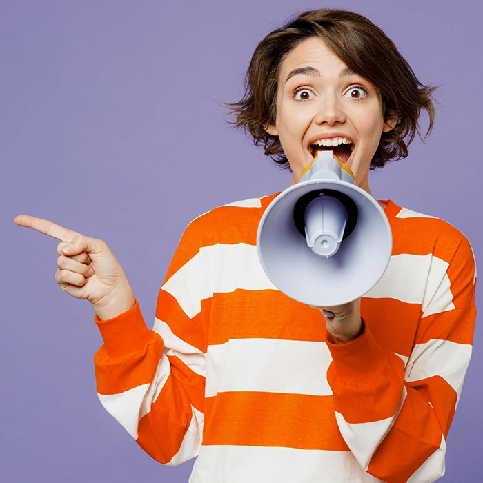 refer-a-friend-vancubers A smiling woman in an orange and white striped shirt holding a megaphone, pointing sideways to highlight VanCubers’ refer-a-friend coworking and virtual office offer.