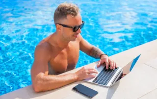 how to keep your business moving while you’re on vacation 1 entrepreneur working remotely by the pool on vacation with laptop – balancing business and travel